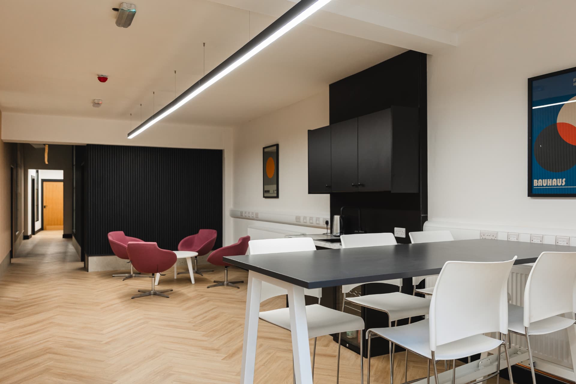 Modern kitchen and breakout area at Patrick's with black cabinets, pink armchairs and high tables